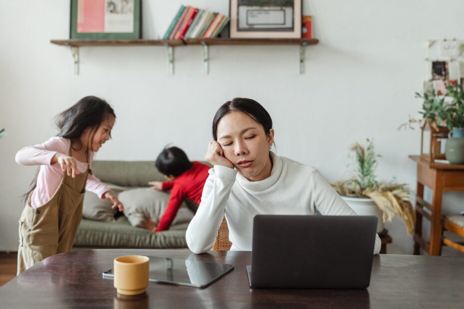 Femme regarde son ordinateur épuisée, ses enfants jouent énergiquement, l'excès de responsabilité conduit à l'épuisement